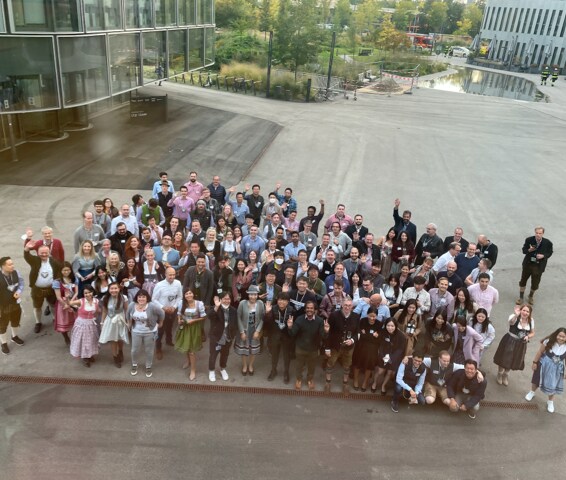 A large group of people gathered outside a modern office building, smiling and waving at the camera in a corporate event setting.