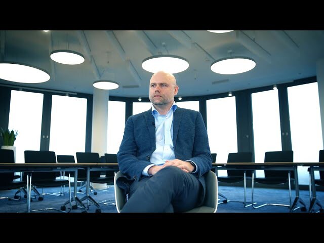 Corporate leader seated confidently in a contemporary meeting space with large windows and modern lighting.