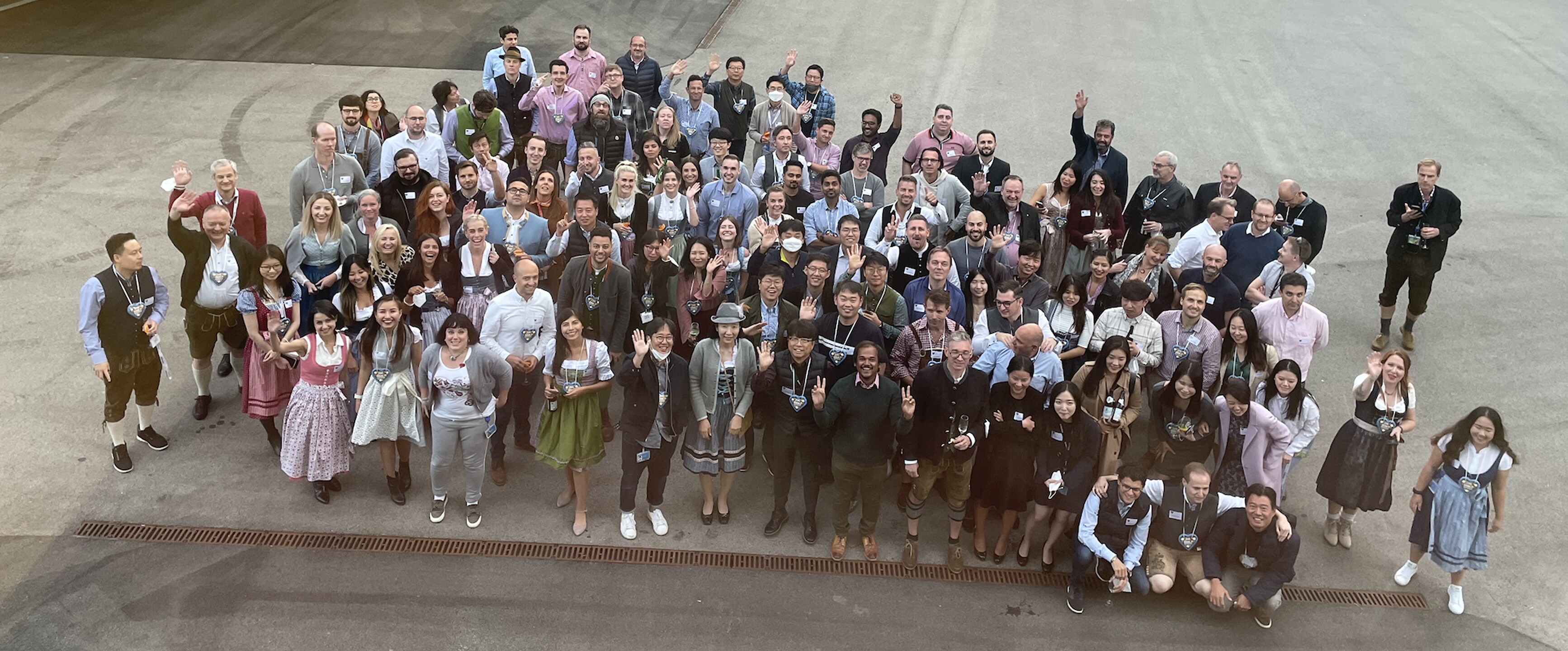 A large group of people gathered outside a modern office building, smiling and waving at the camera in a corporate event setting.