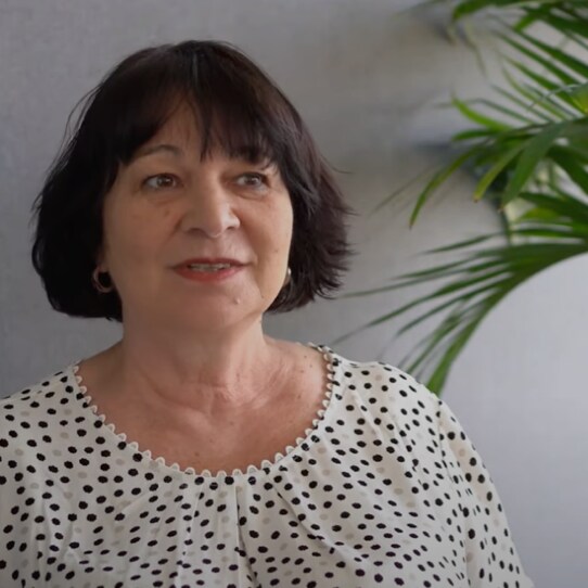 An older woman with short dark hair wearing a white blouse with black polka dots.