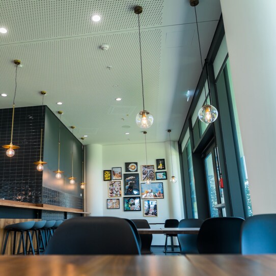 A stylish, modern café interior featuring pendant lights, black tile walls, high stools, and art-covered walls in a cozy, well-lit space.