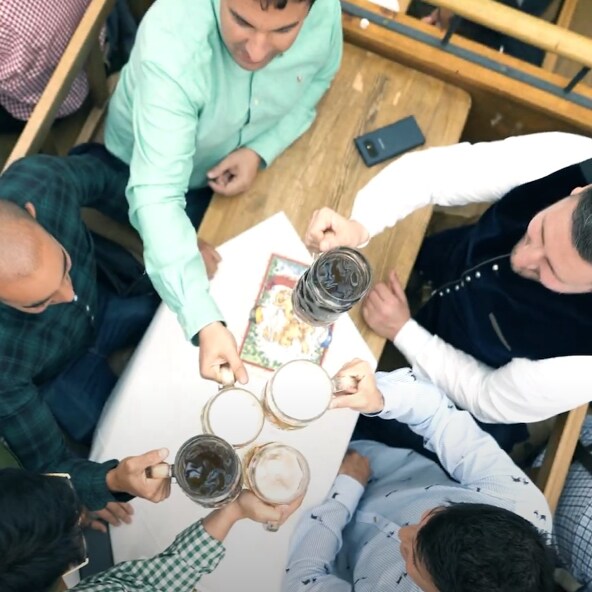 Overhead view of a group of men toasting with beer mugs around a wooden table during a social or festive gathering.