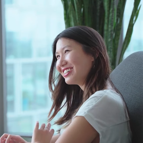 A smiling woman sitting in a modern office chair near a window.