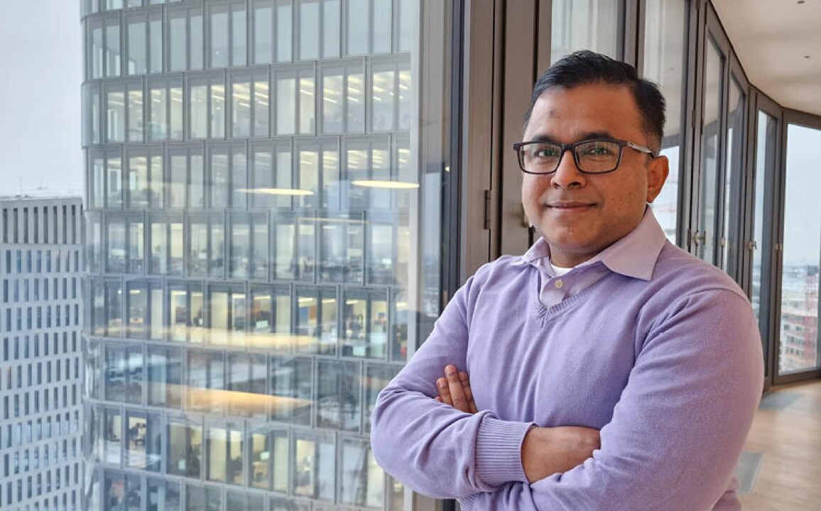 Professional portrait of Helal Morshed, Head of SoC Software, in a lavender sweater with arms crossed, overlooking a modern urban office district.