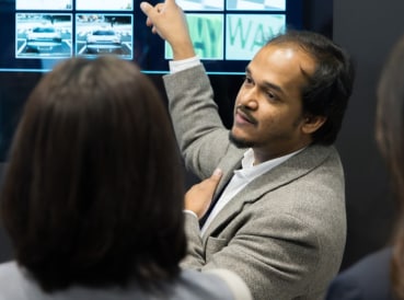 A professional giving a focused presentation, pointing to visual content on a digital display.
