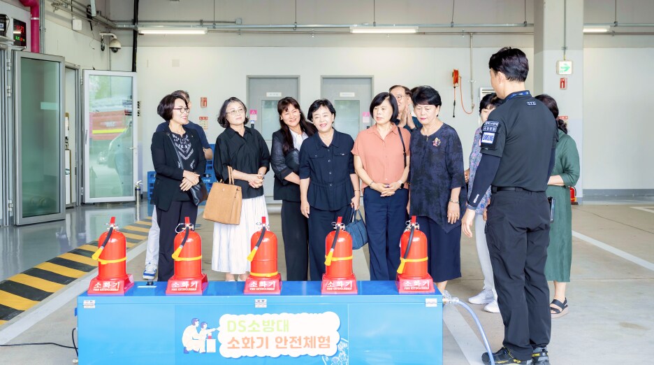 방재센터에서 안전 담당자가 소화기 사용법과 관계 시스템을 설명하고, 위원들이 소화기 체험존 앞에 서서 경청하는 모습
