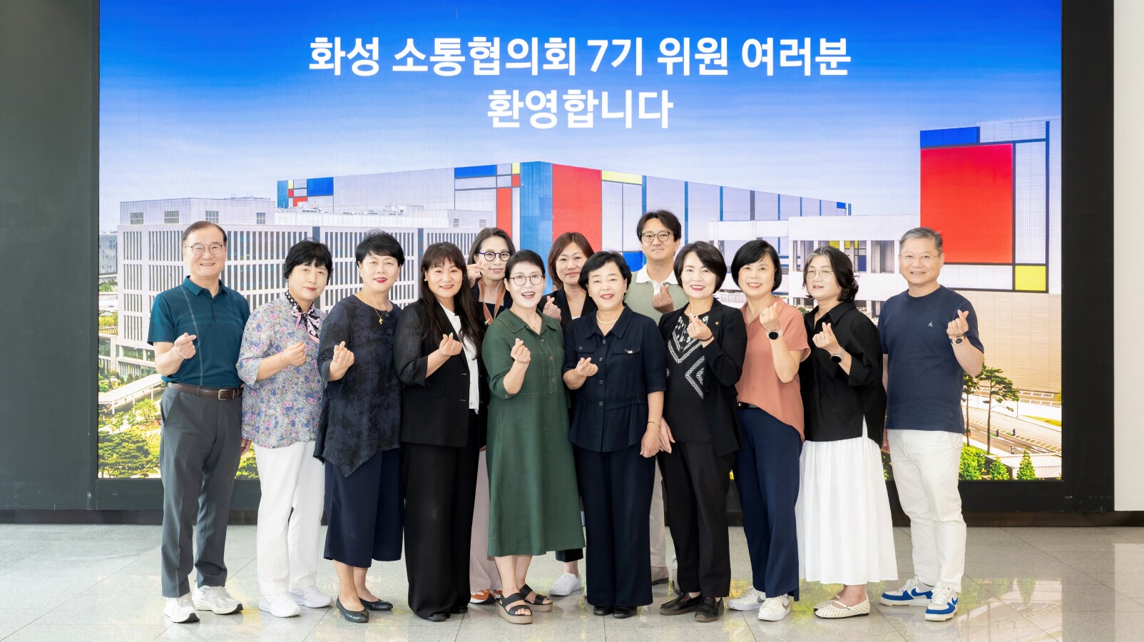 화성 삼성 캠퍼스 화면 앞에서 ‘화성 소통협의회 7기 위원 여러분 환영합니다’ 문구를 배경으로 위원들이 함께 서서 손가락 하트 포즈를 취하며 밝게 웃는 단체사진.