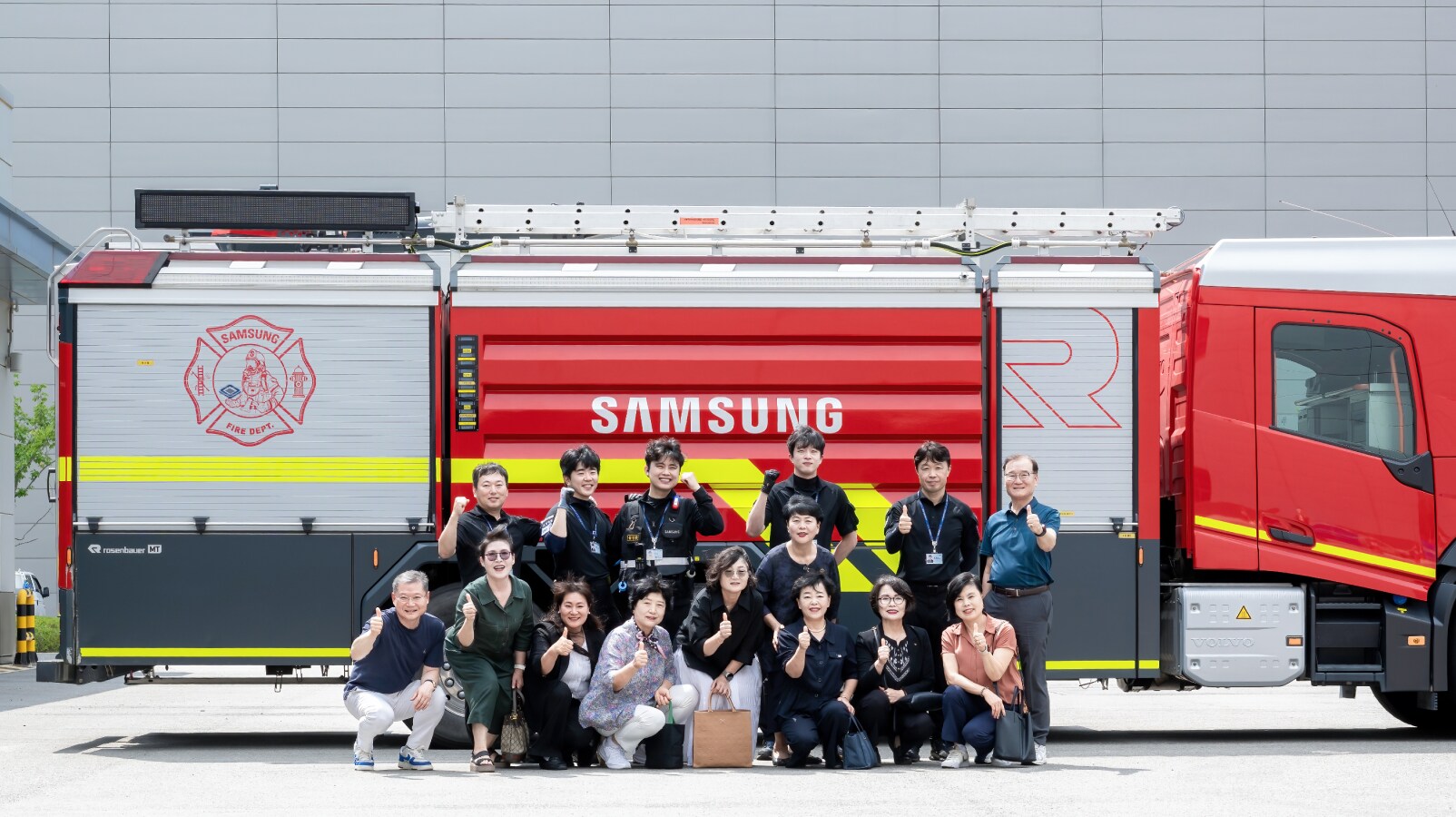 삼성 로고가 새겨진 대형 소방차 앞에서 위원들이 단체로 포즈를 취하며 찍은 기념사진. 남녀 위원들이 줄지어 앉고 서서 밝게 웃고 있다.