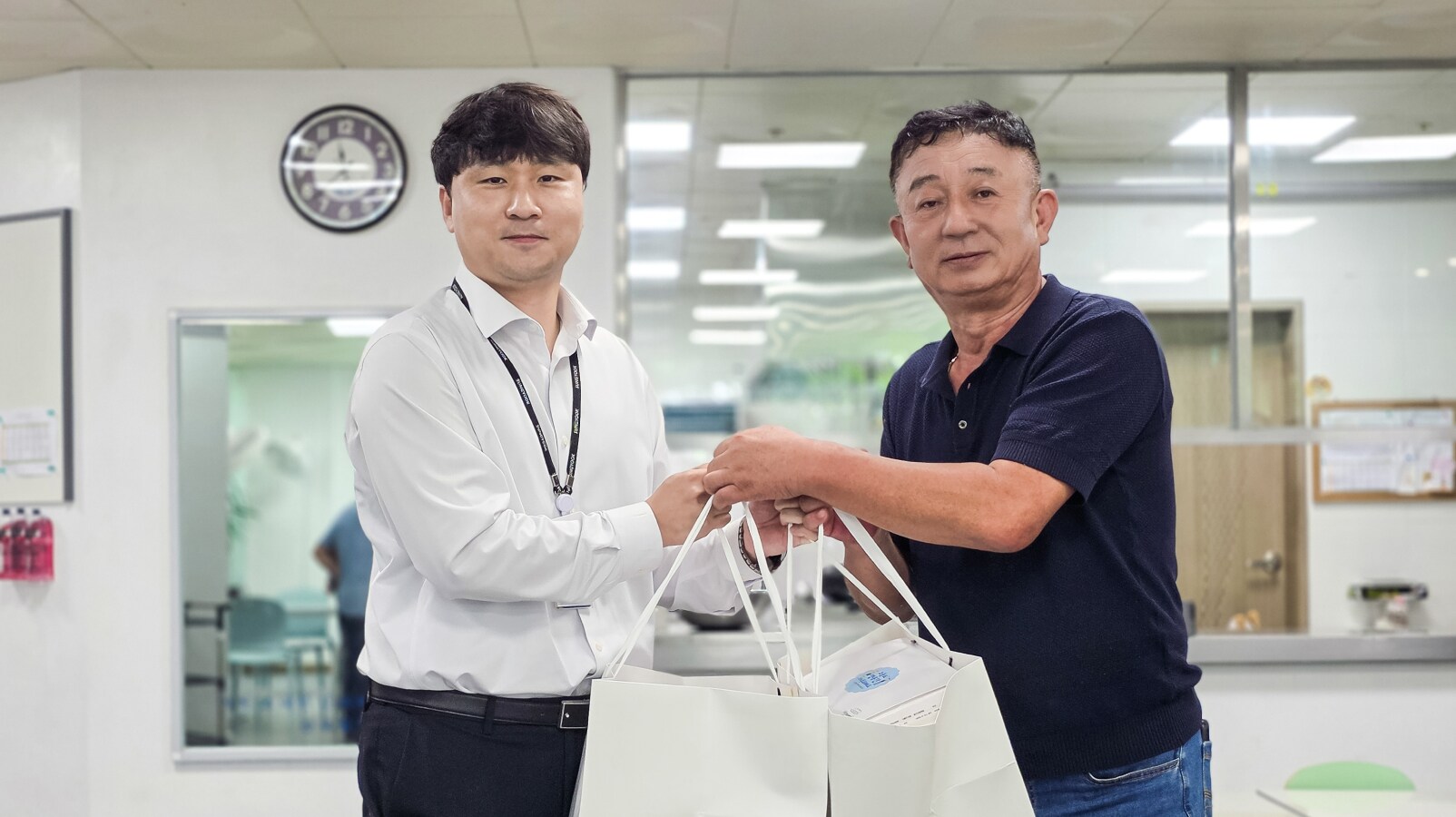 두 남성이 흰색 선물 봉투를 건네며 포즈를 취하고 있습니다.