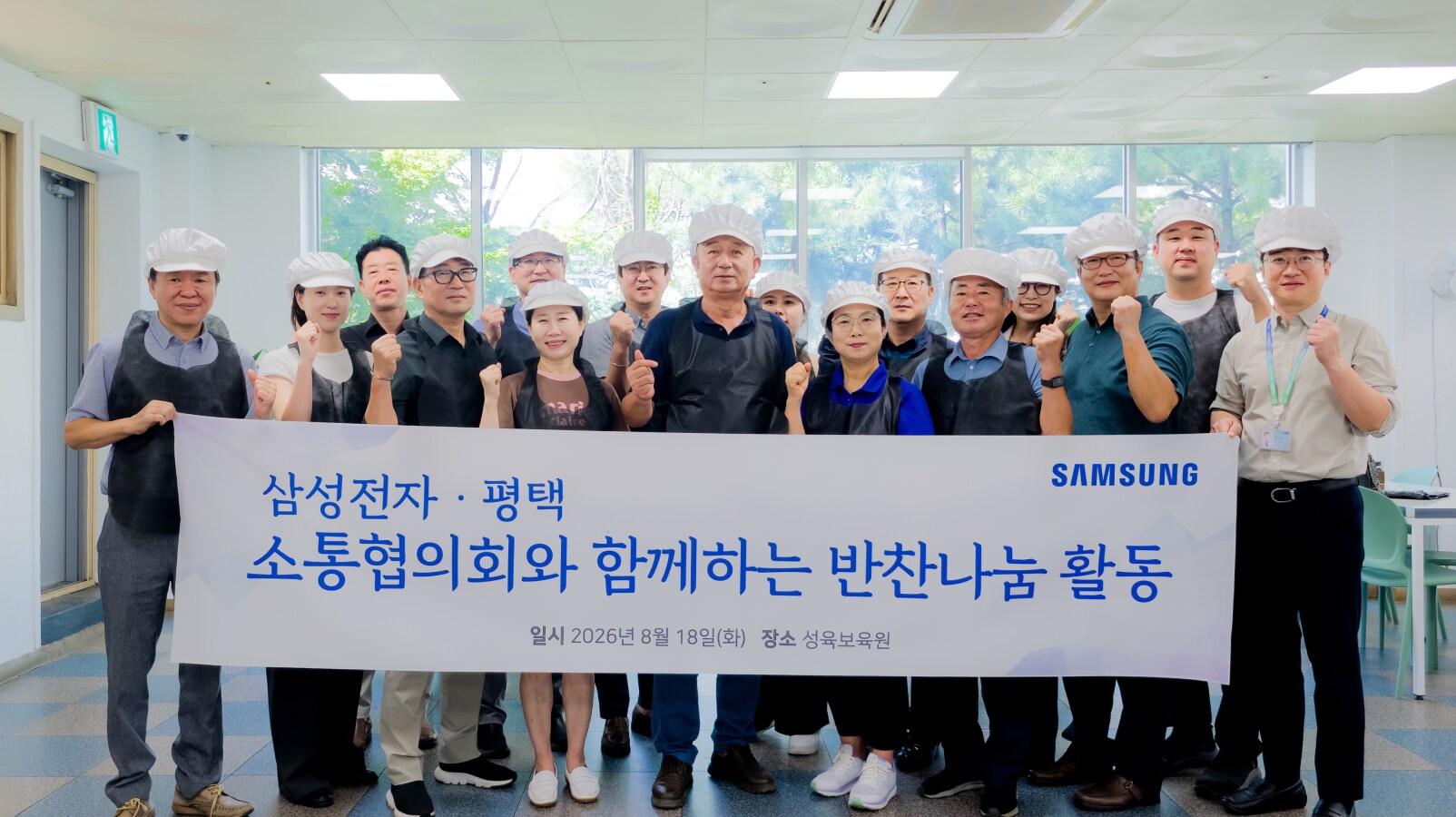 위생모와 앞치마를 착용한 봉사자들이 반찬나눔 활동 현수막을 펼쳐들고 실내에서 포즈를 취하고 있습니다.