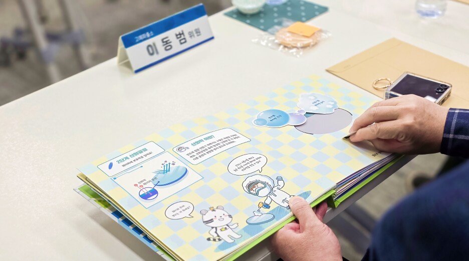 회의 테이블 위에 놓인 희망별숲 제작 팝업북을 참석자가 넘겨 보며 교육 콘텐츠를 확인하는 모습