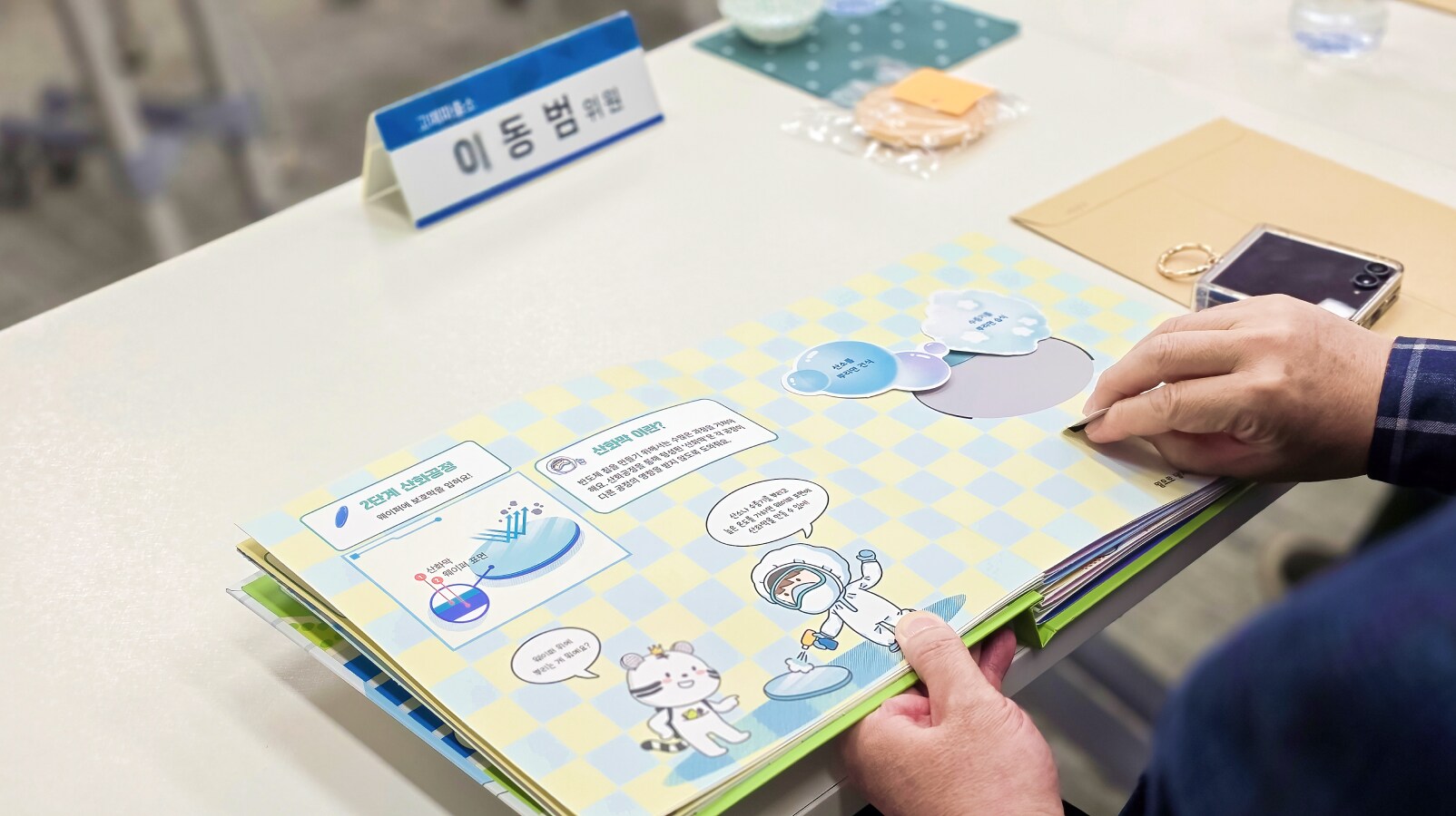 회의 테이블 위에 놓인 희망별숲 제작 팝업북을 참석자가 넘겨 보며 교육 콘텐츠를 확인하는 모습