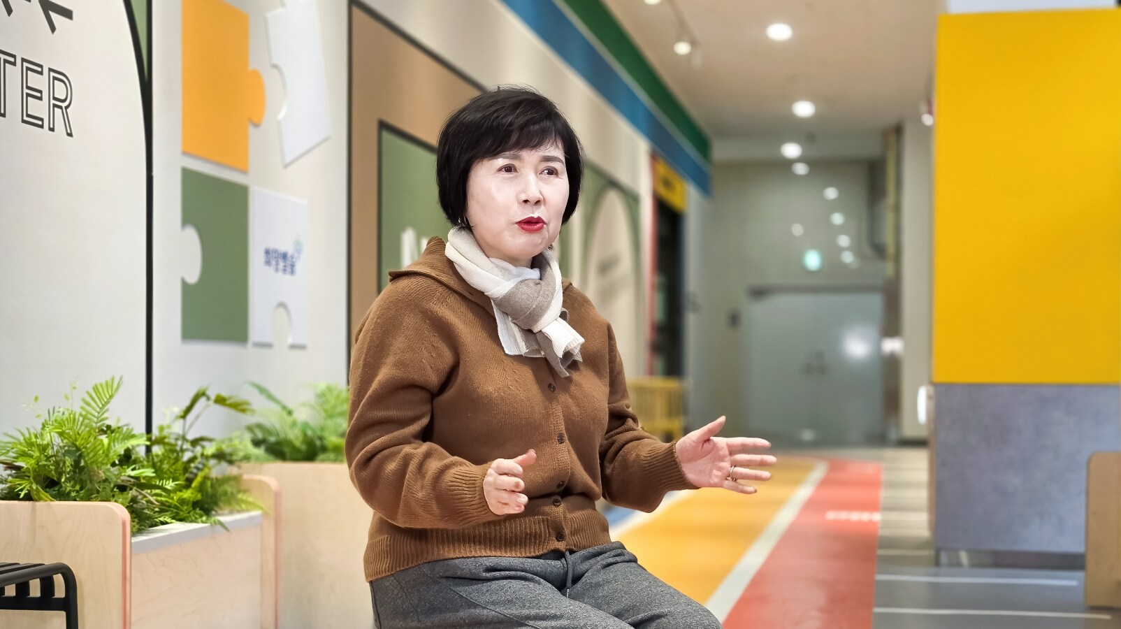 밝은 복도 공간에서 손짓을 섞어 팝업북 체험 소감을 인터뷰로 전하는 이영희 위원