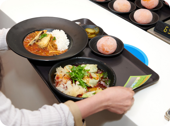 매콤한 국물 요리와 신선한 채소가 올려진 요리가 담긴 식사 트레이를 든 손 모습.