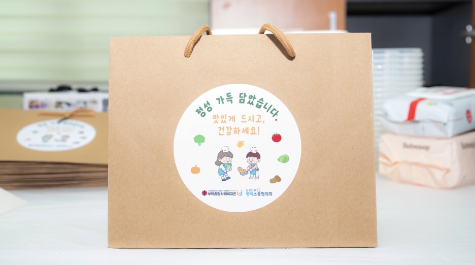 지역사회 나눔 봉사활동을 통해 준비된 반찬 3종과 메시지 카드 세트가 담긴 쇼핑백, 이웃 가정에 전달될 예정인 모습
