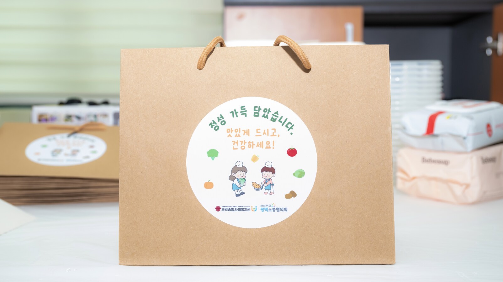 지역사회 나눔 봉사활동을 통해 준비된 반찬 3종과 메시지 카드 세트가 담긴 쇼핑백, 이웃 가정에 전달될 예정인 모습