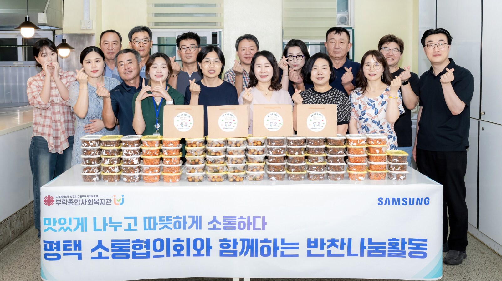 삼성 반찬 나눔 행사에서 지역 주민과 자원봉사자들이 여러 가지 반찬 세트를 준비하고 단체 사진을 찍는 모습
