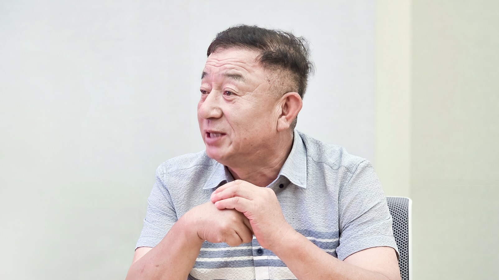 회의실에서 두 손을 모은 채 정면을 응시하며 인사말을 전하는 중년 남성