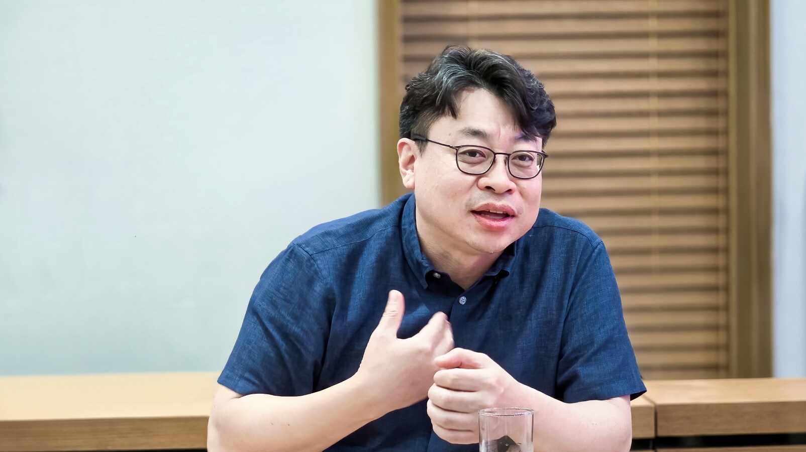 안경을 쓰고 대나무발 배경 앞에서 손짓하며 소감을 밝히는 남성