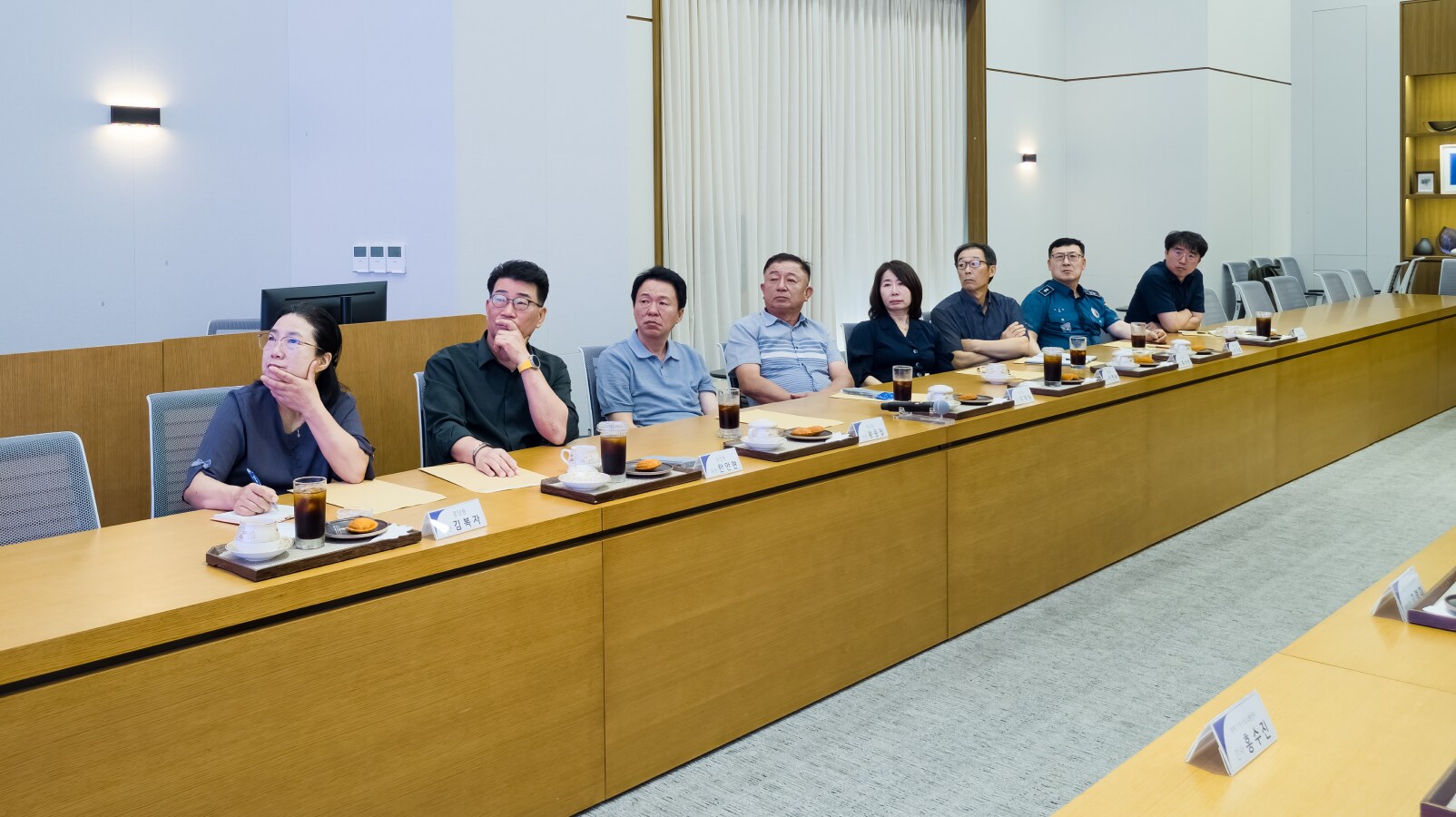 긴 테이블에 나란히 앉아 발표 자료를 바라보며 안건을 경청하는 여러 위원들