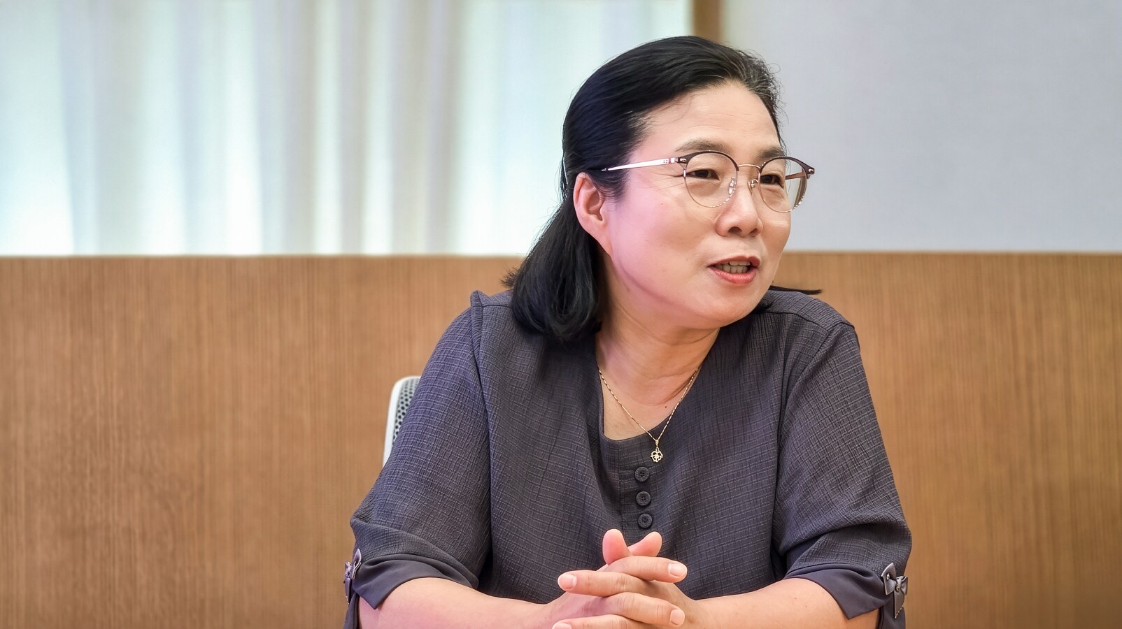 안경을 쓰고 목걸이를 착용한 여성이 두 손을 모은 채 발언하는 장면