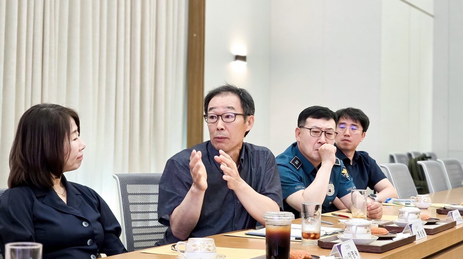 손을 들어 제스처를 취하며 화학물질 고지 사항에 대해 질문하는 남성과 옆에서 경청하는 참석자들