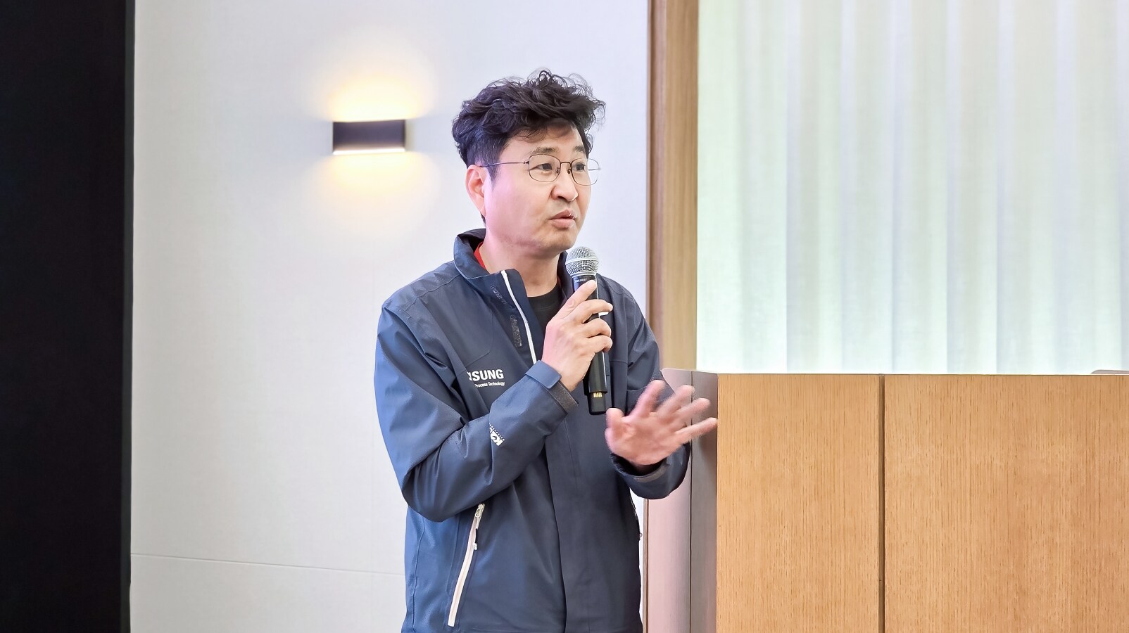 삼성 로고가 새겨진 재킷을 입고 마이크를 든 채 손짓하며 설명하는 남성