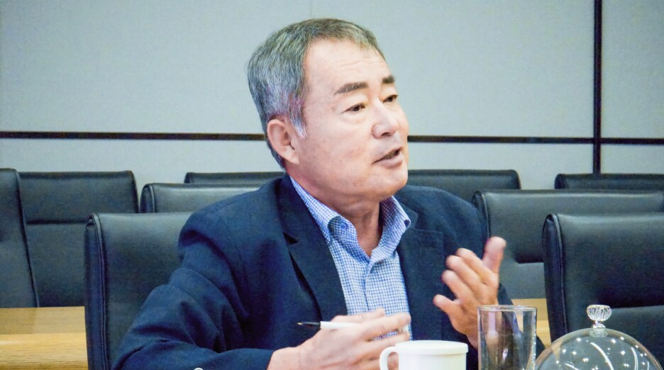 김재환 위원이 회의 중 주민 의견을 전달하며 손짓으로 설명하고 있다. 앞에는 컵과 문서가 놓여 있다.