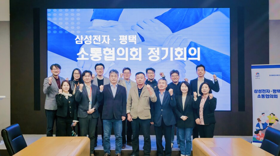 ‘삼성전자·평택 소통협의회 정기회의’ 화면 앞에서 참석자들이 함께 서서 주먹을 쥐고 포즈를 취하고 있다. 모두 밝은 표정으로 단체 사진을 촬영하고 있다.