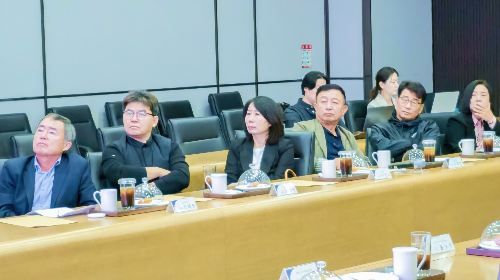 회의실에서 소통협의회 위원들이 자료를 보며 화학사고 예방관리 계획서 발표를 진지하게 경청하고 있다. 테이블 위에는 음료와 문서가 놓여 있다.