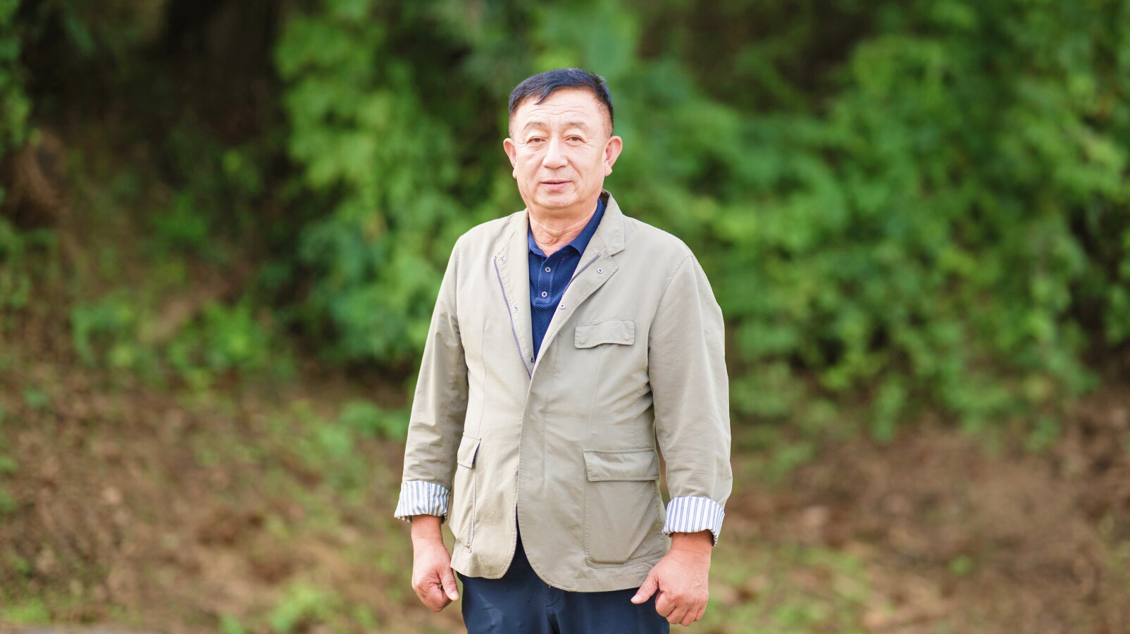 푸른 나무가 배경으로 보이는 야외에서 우제욱 대표위원이 정면을 바라보며 서 있는 모습. 밝은 표정으로 카메라를 향해 자연스럽게 포즈를 취하고 있다.