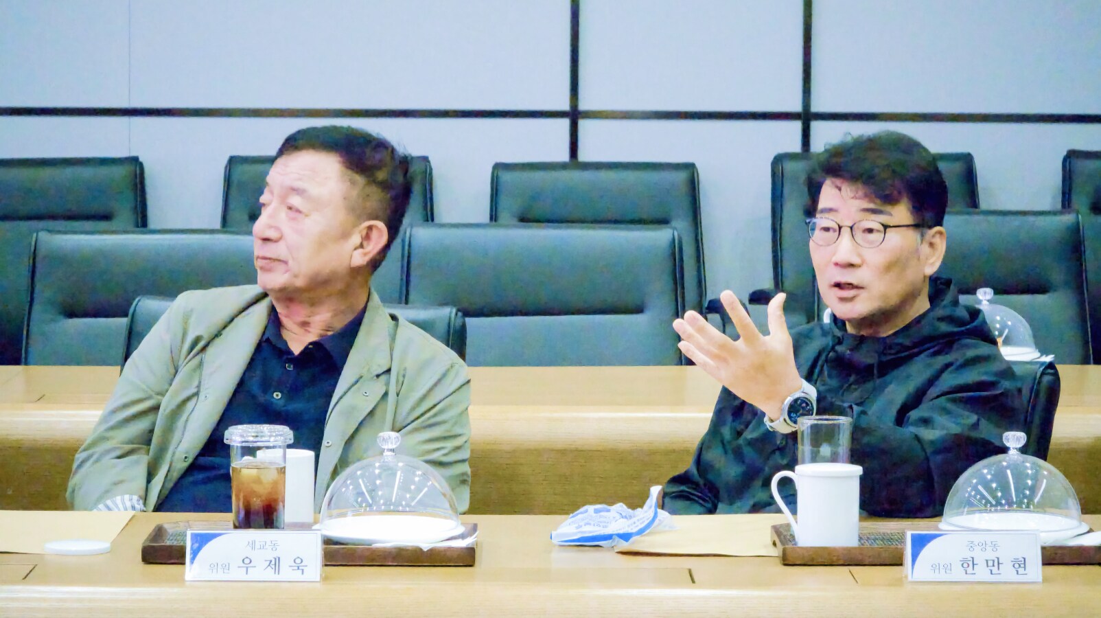 우제욱 대표위원(왼쪽)과 한만현 위원(오른쪽)이 분동 관련 사안에 대해 의견을 나누며 진지하게 대화하고 있다. 테이블 위에는 음료와 자료가 정돈되어 있다.