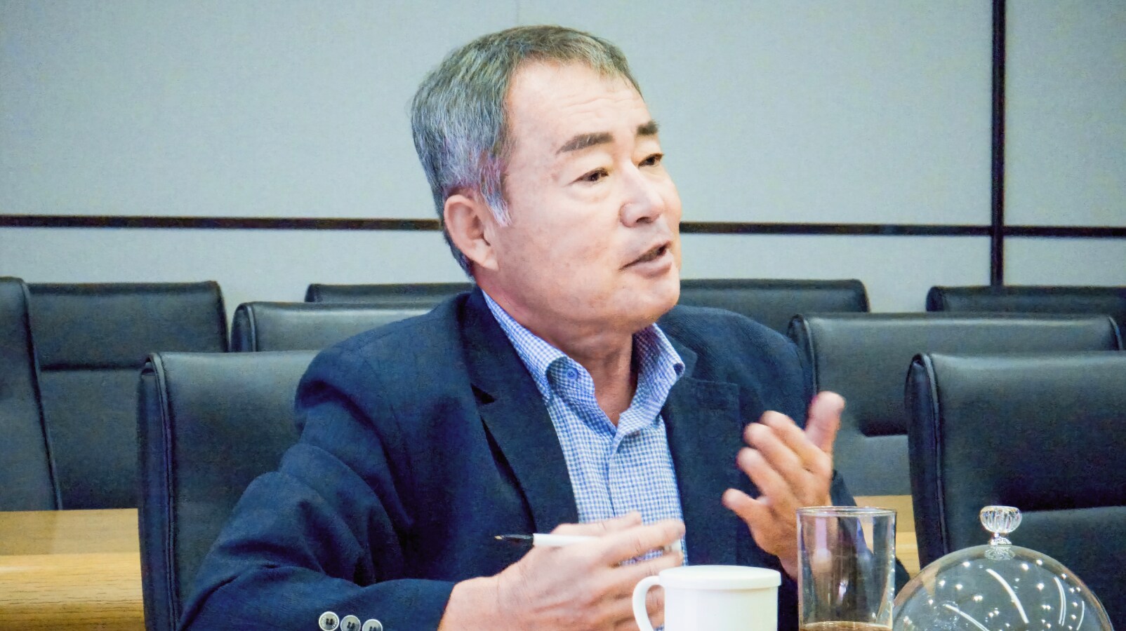 김재환 위원이 회의 중 주민 의견을 전달하며 손짓으로 설명하고 있다. 앞에는 컵과 문서가 놓여 있다.