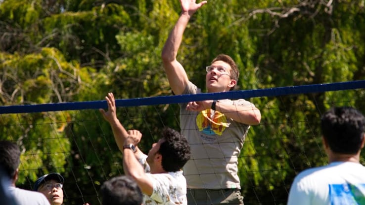 SARC/ACL internship students playing volleyball outdoors, with one student jumping to spike the ball.