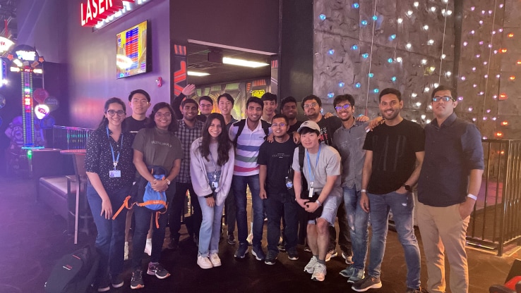 SARC/ACL internship students posing together at an indoor amusement location, with colorful lights and laser tag signs in the background.