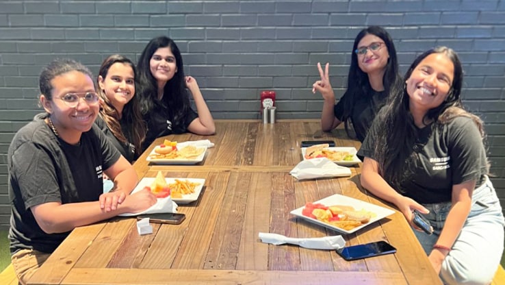 SARC/ACL internship students enjoying their free daily lunch, seated around a wooden table with plates of food.