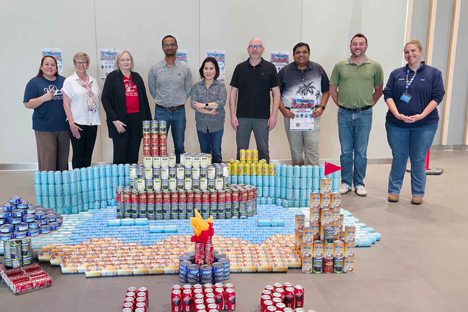 A team of Samsung employees standing and smiling behind a large canned-food structure, representing a corporate community outreach or charity competition.
