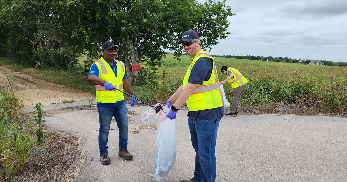 Employees remove litter from a roadside area during a community volunteer effort focused on environmental sustainability.