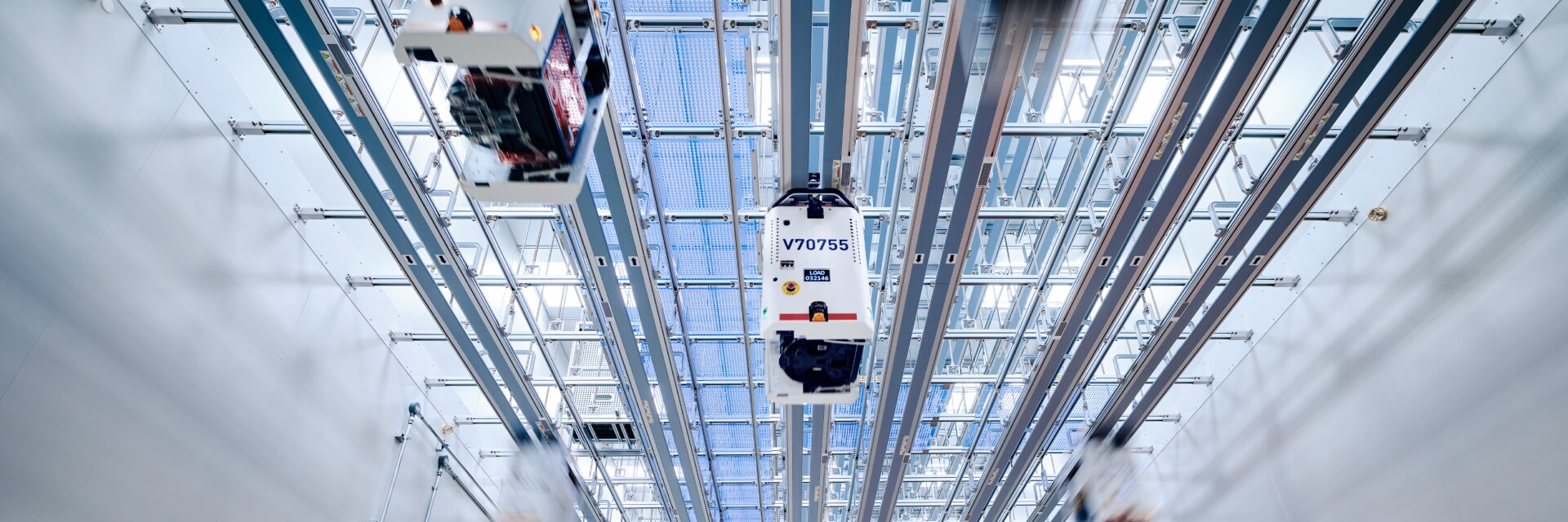 Ceiling-mounted transport robots moving along rail tracks inside a clean facility.