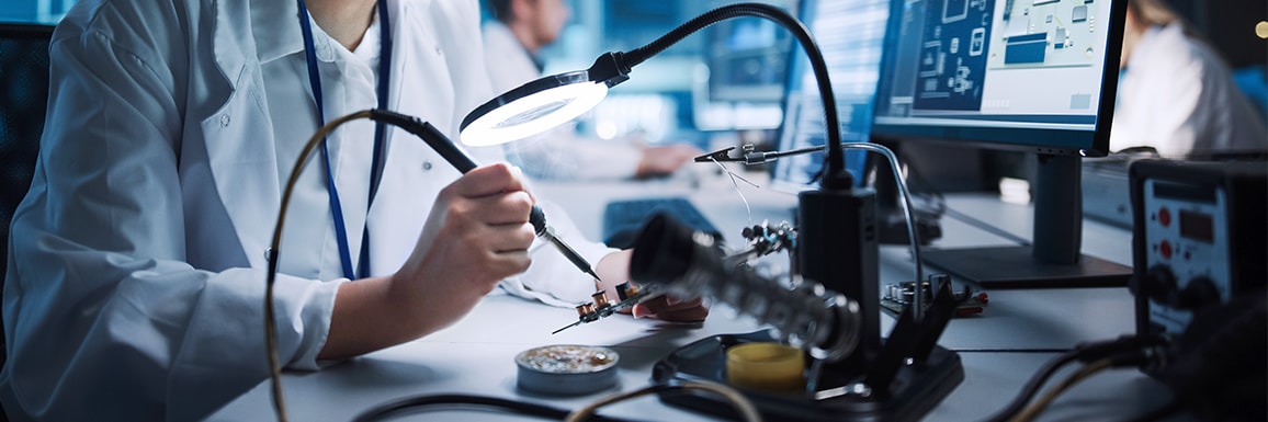 A close-up of an engineer soldering a circuit under a magnifying lamp in a modern laboratory.