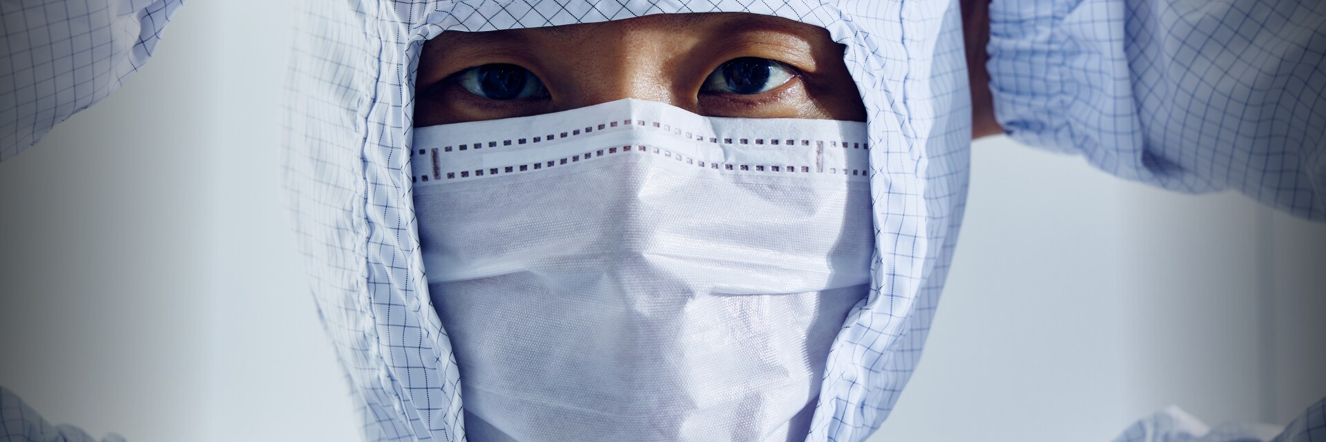 A close-up image of a cleanroom technician wearing a protective hood and mask