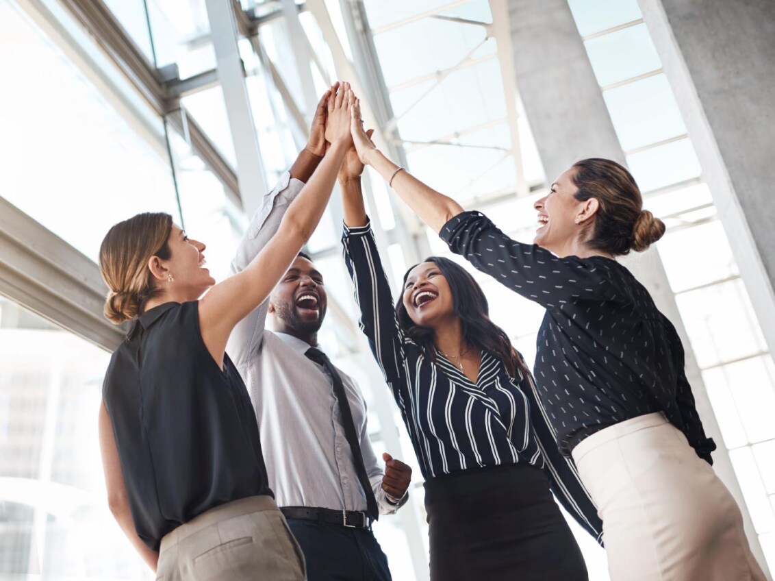 Diverse group of smiling business professionals giving a high five in a bright, modern office setting.
