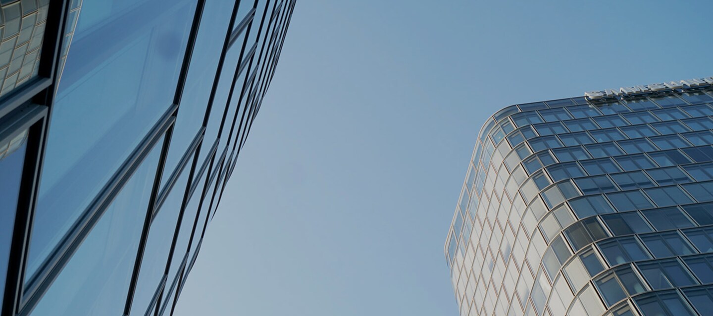 Upward view of two modern glass office buildings against a clear blue sky, showcasing sleek architectural design.