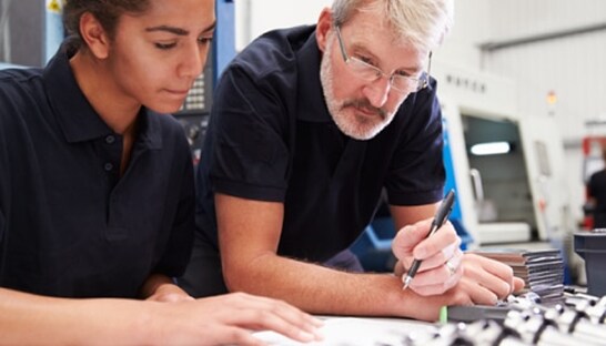 Two engineers in a manufacturing environment reviewing technical schematics.