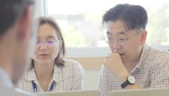A man and a woman collaborate during a meeting, both looking attentively at their laptops in a bright workspace.