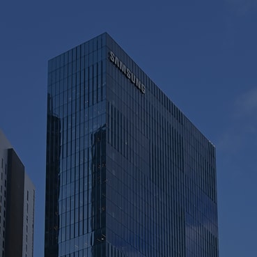 Upward‑angled view of Samsung’s office building, featuring a modern glass façade against a clear blue sky.