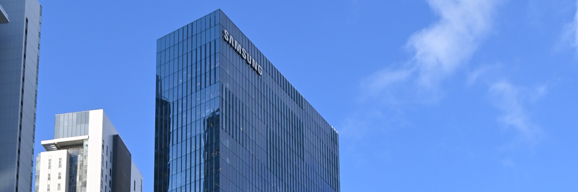 Upward‑angled view of Samsung’s office building, featuring a modern glass façade against a clear blue sky.