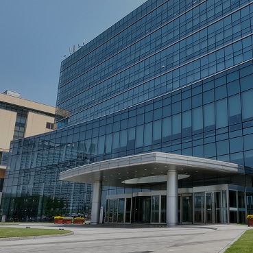 A modern Samsung office building with a sleek glass façade and a prominent main entrance, set against a clear blue sky.