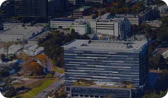 Aerial view of a Samsung office building in Korea, featuring a sleek, horizontal glass façade and a rooftop garden amidst an urban landscape.