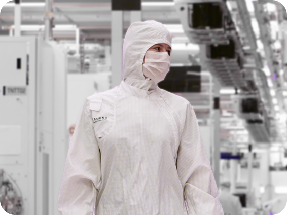 A Samsung Semiconductor employee in full cleanroom attire, working inside a sterile fabrication facility surrounded by advanced manufacturing equipment.